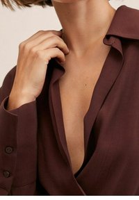 Bordeaux-paita, jossa on syvä V-mallinen kaula-aukko, jämäkkä kaulus ja nappidetaljit hihoissa. Kangas vaikuttaa sileältä ja kevyeltä.