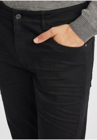 Mustad denimipüksid otse lõikega, millel on esikott ja ülemise nööbi detail. Kanga tekstuur on sile ja minimaalsete kulumismärkidega.