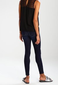 Haut noir sans manches avec un panneau texturé, assorti à un jean skinny bleu foncé et des sandales slide métalliques ornées de broderies.