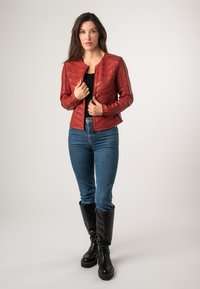 Rode leren jack met horizontale stiksels, aansluitend ontwerp, ronde halslijn en ritssluiting. Gecombineerd met blauwe jeans en zwarte laarzen tot de knie.