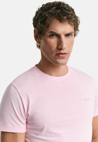 Lichtroze katoenen T-shirt met een ronde halslijn en korte mouwen. Klein groen logo op de borst. Soepele textuur, casual ontwerp.