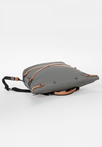 Grau Rucksack mit sleekem Design und tanfarbenen Lederakzenten. Verfügt über verstellbare Träger, einen oberen Griff und eine glatte, matte Oberfläche.