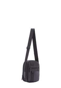 Borsa a tracolla in nylon nero con tracolla regolabile. Presenta scomparti con zip, tessuto testurizzato e dettagli con logo. Forma rettangolare compatta.