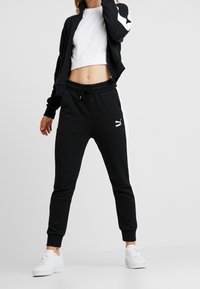 Svart träningsoverallsjacka med vita detaljer och en croppad vit t-shirt, tillsammans med svarta sweatpants med dragsko och vita sidränder.