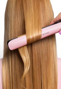 GHD Gold Haarglätter mit einem pinken Gehäuse und schwarzen Keramikplatten, die glänzendes, glattes, blondes Haar stylen. Nahaufnahme des laufenden Stylings.