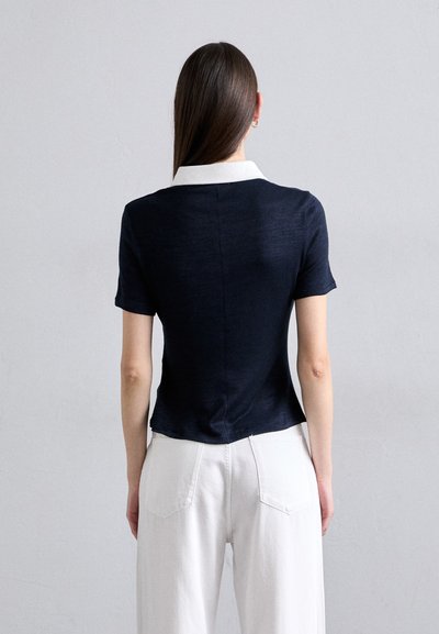 Navy short-sleeved top with a white collar, fitted design, and soft texture. Back view shows clean lines and a subtle seam detail.