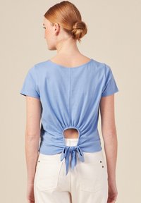Top azzurro chiaro a maniche corte con scollatura rotonda e parte posteriore arricciata con apertura a chiave, legato in vita con un tessuto coordinato.