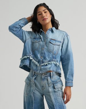 Vrouw die een cropped spijkerjack met versleten zoom en high-waisted spijkerbroek met zakken poseert, met één hand die haar haar raakt.