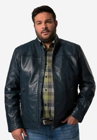 Mörkblå läderjacka med dragkedja fram, ståkrage och två sidofickor. Bärs över en rutmönstrad skjorta med strukturerad yta.