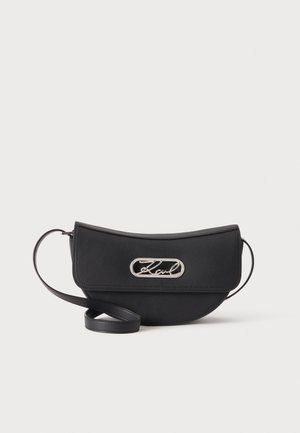 Zwarte halvemaanvormige crossbodytas met klep en zilveren metalen detail met een kenmerkend logo, tegen een effen witte achtergrond.