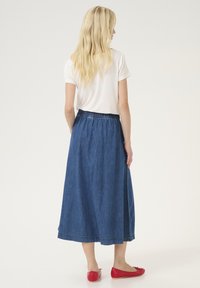 Jeans maxi krilo z elastičnim pasom. Tkanina je srednje modre barve, z gladko teksturo in robom z diskretnim šivom.