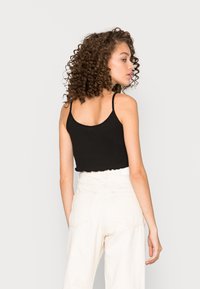 Top cropped preto com nervuras e alças finas, com uma bainha rendada. Combinado com calças de cintura alta de cor clara.
