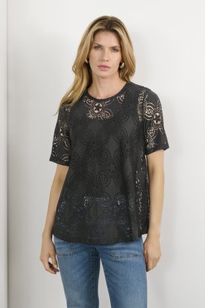 Svart spetsblus med blommönster, korta ärmar, rund halsringning, transparent struktur. Bärs över blå jeans med avslappnad passform.