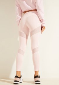 Leggings de entrenamiento rosas con un diseño suave y ajustado. Presentan paneles de malla en los lados y una cinturilla alta. Combinados con zapatillas deportivas.