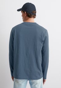 Langärmliges Hemd aus weichem blauen Stoff mit lockerer Passform. Mit Rundhalsausschnitt und geradem Saum. Kombiniert mit hellen Jeans.