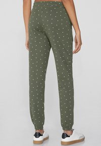 Joggers de color verde oliva hechos de una tela suave, con un patrón de lunares blancos, cintura elástica y puños elásticos, combinados con zapatillas blancas.