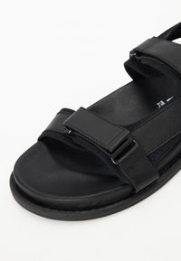 Sorte sandaler med to justerbare stropper, glatt lærtekstur, rund tåform og flat gummisåle.