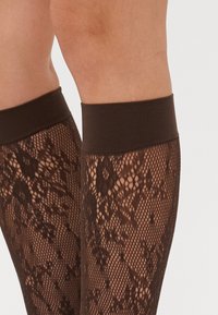 Calze autoreggenti marroni con un motivo testurizzato e una fascia piuttosto scura in cima, che mette in evidenza un delicato design in rete.
