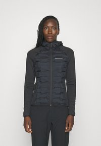 Sort jakke med en fyldt isoleret front og tætsiddende ærmer. Har hætte, lynlås lukning og logo på brystet. Glat tekstur.