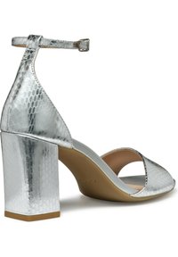 Zilveren sandalen met hoge hakken en een blokhak, met een gestructureerd slangenhuidpatroon en een enkelband met een metalen gesp.