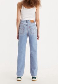 Light blue straight-leg jeans with a high waistband, featuring back pockets and curved stitching detail, worn with a white tank top.