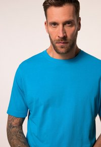 T-shirt in cotone turchese con maniche corte, scollatura rotonda e texture liscia, caratterizzato da un design aderente e uno stile minimalista.