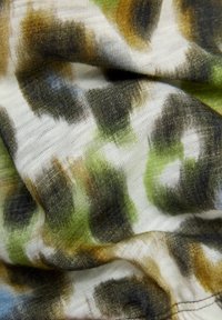 Nahaufnahme eines Stoffes mit grünem, braunem, schwarzem und weißem Tarnmuster sowie sichtbarer Strickstruktur und Falten.