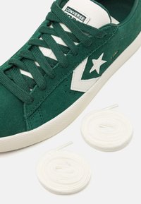 Green suede sneaker with white rubber sole and leather accents. Features white star logo and matching laces, highlighting texture and contrast.