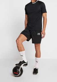 Svart idrottströja med korta ärmar, i kombination med matchande svarta shorts. Svarta fotbollsskor på en svart boll med vita och röda detaljer.