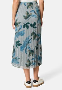 Bloemenplissé midi-jurk in lichtblauw, met een verticale gestreepte print en groene bladeren. Gekozen met witte sneakers en zwarte accenten.