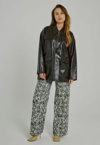 Mustu, läikiv, ülisuur faux nahk jakk, millel on krae ja taskud, kombineeritud mustade ja valgete mao mustriga laiapõhjaliste pükstega.