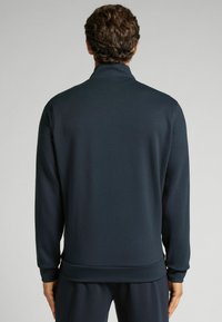 Sudadera con cremallera de color azul marino oscuro, con cuello alto, mangas largas y puños y dobladillo acanalados, fabricada en una tela suave y elástica.