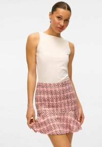 Haut sans manches blanc associé à une jupe en tweed rose avec un motif à carreaux et un ourlet volé. Texture lisse, design ajusté.