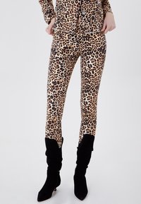 Leggings de estampado de leopardo en beige y negro, con un diseño ajustado y una textura suave. Combinados con botas altas negras y texturizadas.