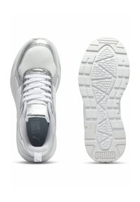 Weiße Sportschuhe mit strukturiertem Obermaterial, metallisch silbernen Akzenten, flachen Schnürsenkeln und einer gemusterten weißen Sohle. Puma-Logo auf der Zunge und Ferse.