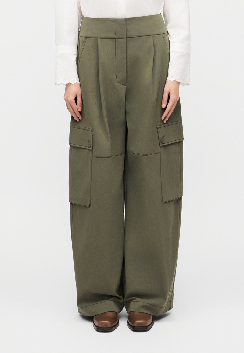 Pantalon cargo vert olive à jambes larges, doté de deux poches avant, d'une taille haute et d'une texture de tissu lisse. Associé à des chaussures marron.