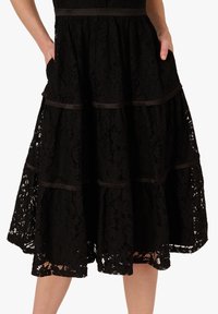 Abito nero in pizzo con design a strati, caratterizzato da rifiniture in satin e tasche. Il tessuto presenta un motivo floreale e una finitura textured.