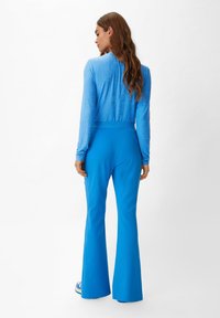 Top blu lungo a maniche con motivo testurizzato e pantaloni a palazzo abbinati, entrambi in un blu solido vivace. Il materiale sembra liscio ed elasticizzato.