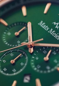 Cadran de montre vert avec aiguilles et sous-cadrans en ton doré, finition texturée, une fenêtre de date et le nom de la marque "Mats Meier" en blanc.