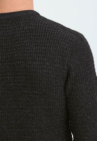 Sort strikket sweater, tekstureret stof, design med rund hals, tæt på blik af ryggen som viser detaljeret syning og ribbet kant.