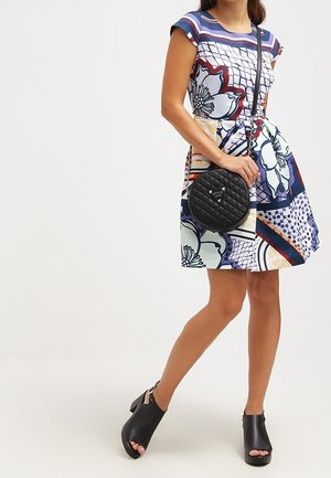 Bolso de mano circular acolchado negro combinado con un vestido de manga corta de estampado colorido que presenta diseños florales y rayas. Sandalias de plataforma negras.