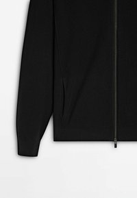 Giacca nera con zip in tessuto a maglia testurizzata, caratterizzata da una forma dritta, tasche laterali e dettagli con zip in metallo.