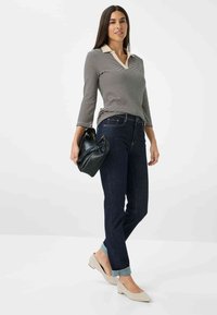 Gestreiftes Langarm-Polo mit beigem Kragen, kombiniert mit dunkelblauen Jeans, die an den Bündchen gerollt sind, und beigen Ballerinas. Schwarze Handtasche als Akzent.