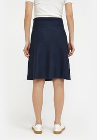 Jupe bleu marine, longueur genou, avec une taille ajustée et un bas évasé. Tissu texturé, fentes latérales, associée à des baskets blanches pour le contraste.