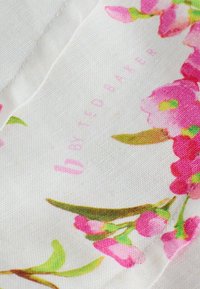 Tissu blanc à imprimé floral rose avec des feuilles vertes, comportant un texte de marque "by Ted Baker" en rose pâle.