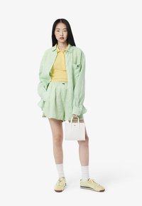 Grön och vit randig skjorta, gul polo, matchande shorts, vit handväska och gula sneakers med blå accenter.