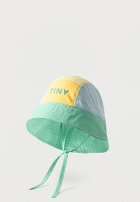 Chapeau seau à blocs de couleurs avec des panneaux jaune, bleu clair et vert menthe, texte "TINY" sur le panneau jaune, et des lanières menthe attachées en nœud sous le menton.