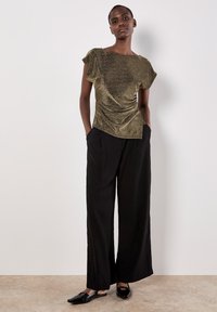 Top corto metallico dorato con design arricciato laterale, abbinato a pantaloni larghi neri a vita alta e scarpe nere lucide.