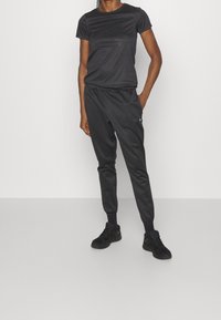 Svart sportig outfit bestående av en åtsittande T-shirt med kort ärm och smala joggerbyxor, båda i ett mjukt tyg med elastisk midja.