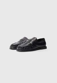 Mocasines de cuero negro con una superficie lisa, punta redondeada, detalles de flecos y un perfil bajo. Diseñados con un estilo deslizable.